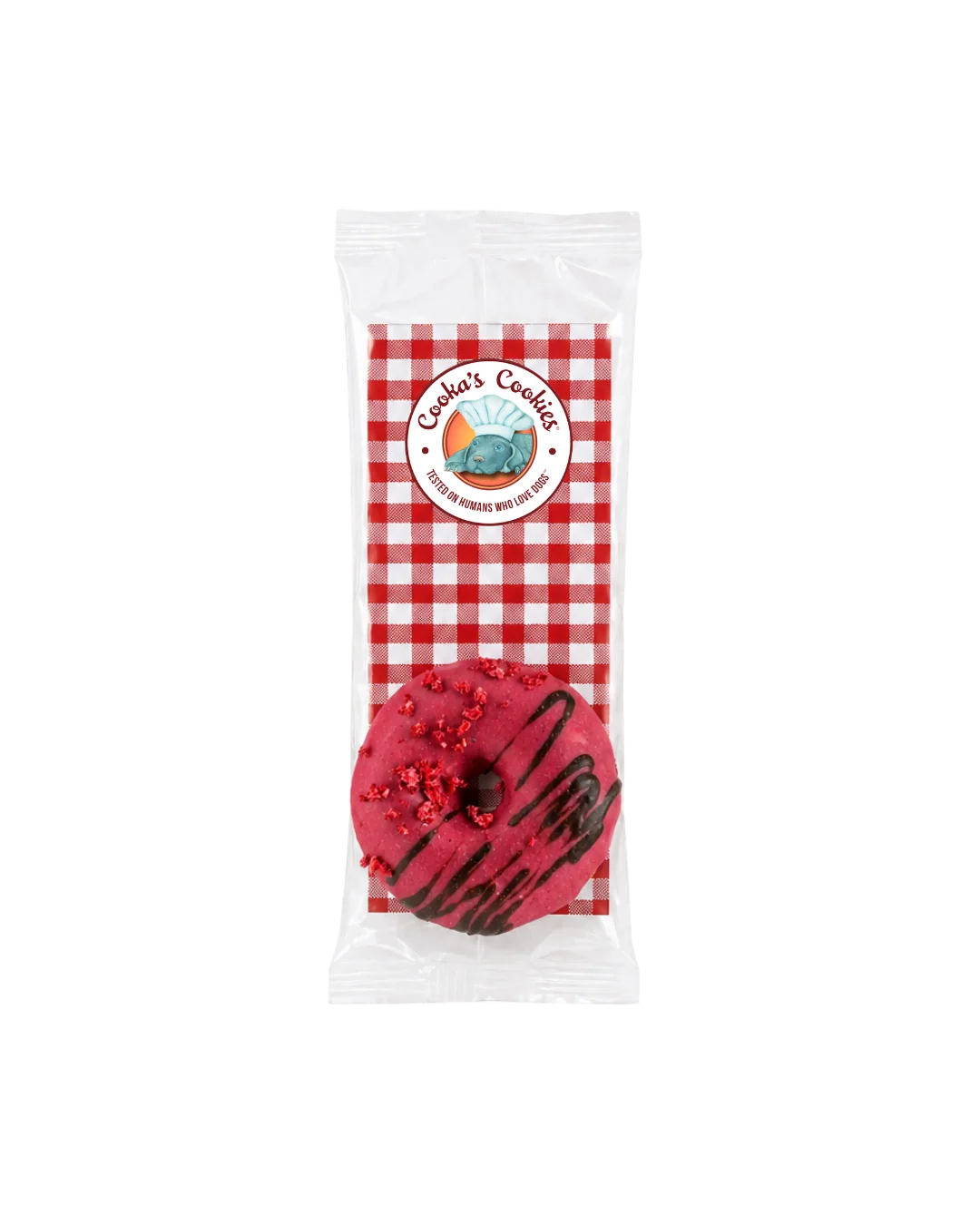 Donutförmiges Hundeleckerli in transparenter Verpackung, rosa glasiert mit roten Krümeln und dunkler Schokoladenlinie; oben rundes „Cooka’s Cookies“-Etikett auf rot‑weiß kariertem Hintergrund.