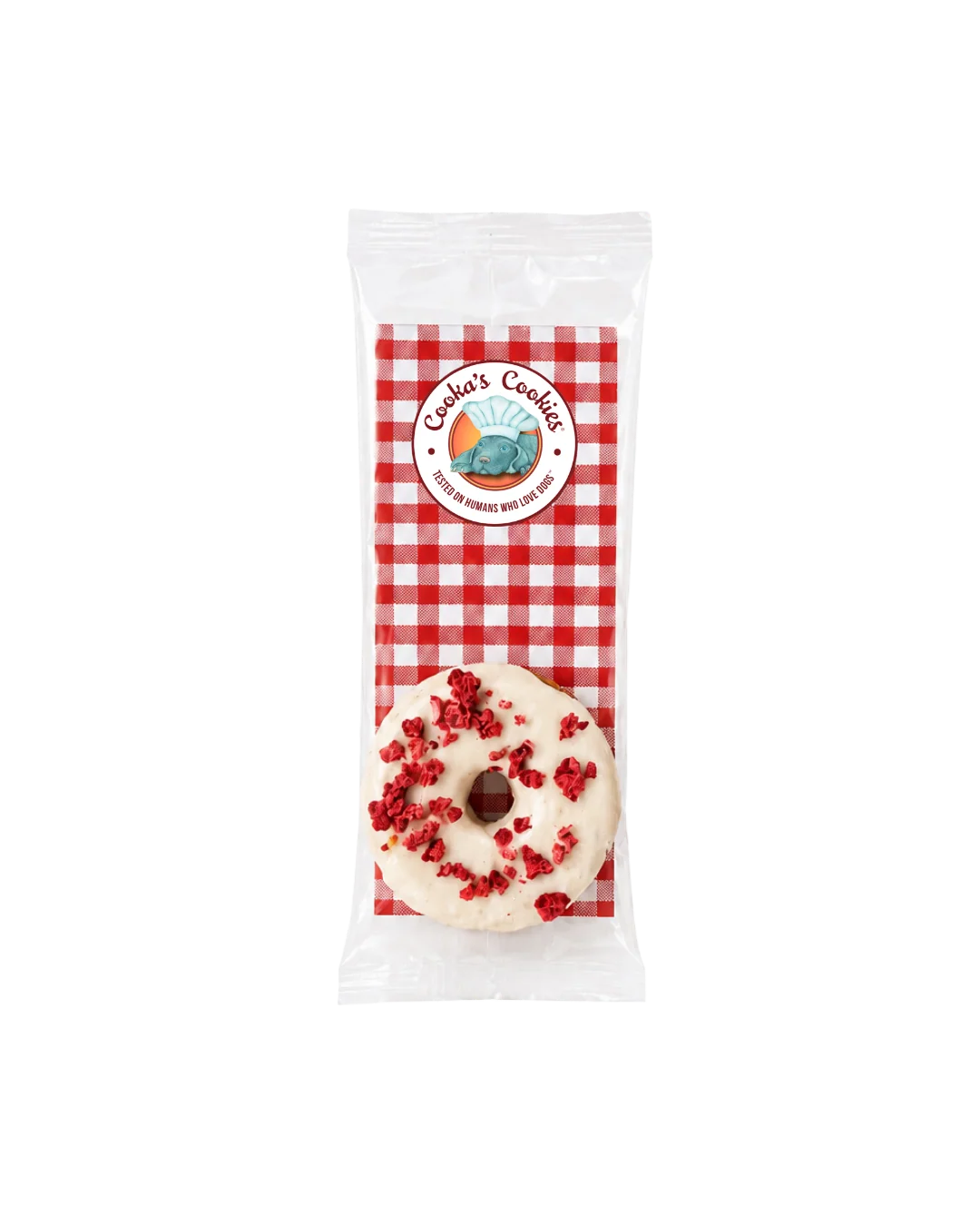 Donutförmiges Hundeleckerli in transparenter Verpackung, weiss glasiert mit roten Krümeln und dunkler Schokoladenlinie; oben rundes „Cooka’s Cookies“-Etikett auf rot‑weiß kariertem Hintergrund.