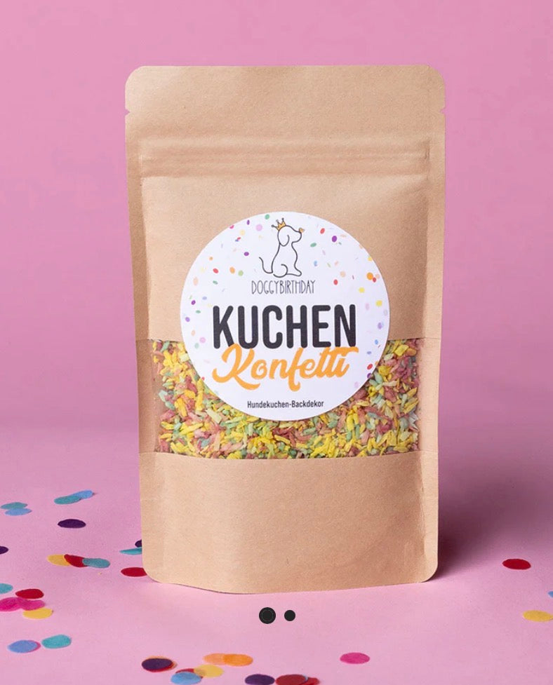Eine Verpackung mit Hundekuchendeko auf einem rosa Hintergrund mit Komfetti 
