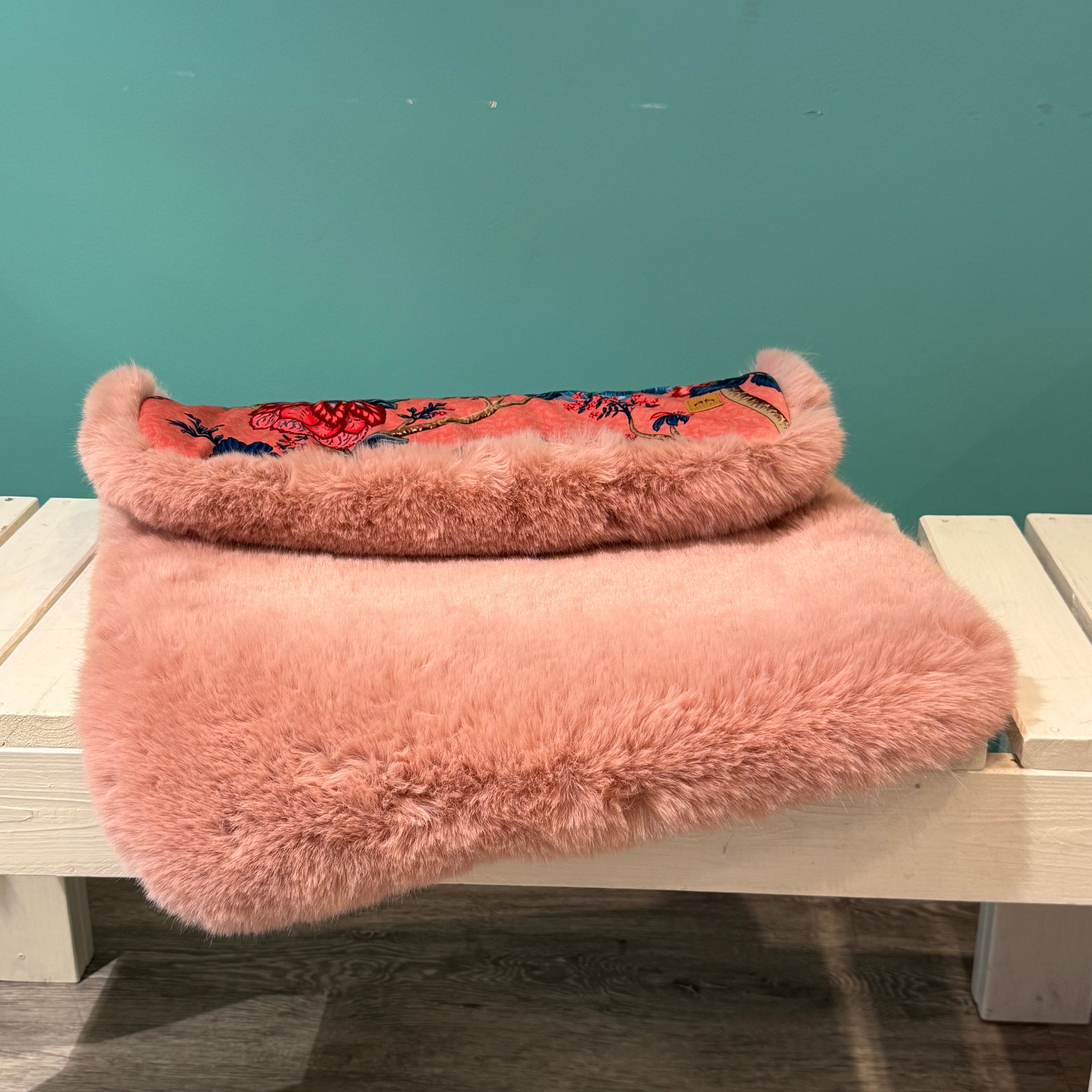 Eine Hundedecke mit Kunstfell in Rosa auf einer weißen Bank 