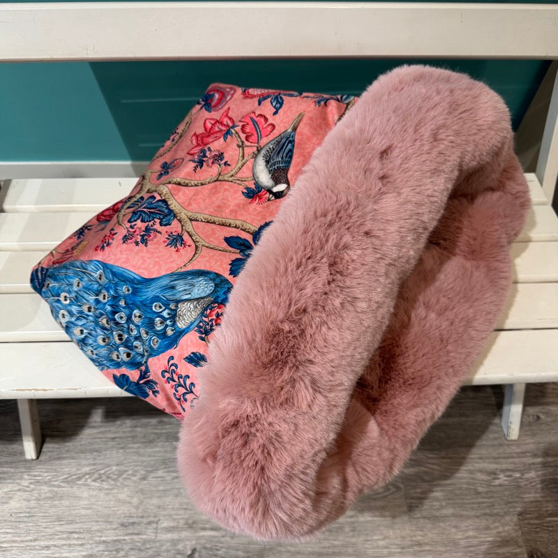 Kuschelhöhle für Hunde seitlich auf einer Bank liegend. Pfau und Meisenmuster auf rosa Grund