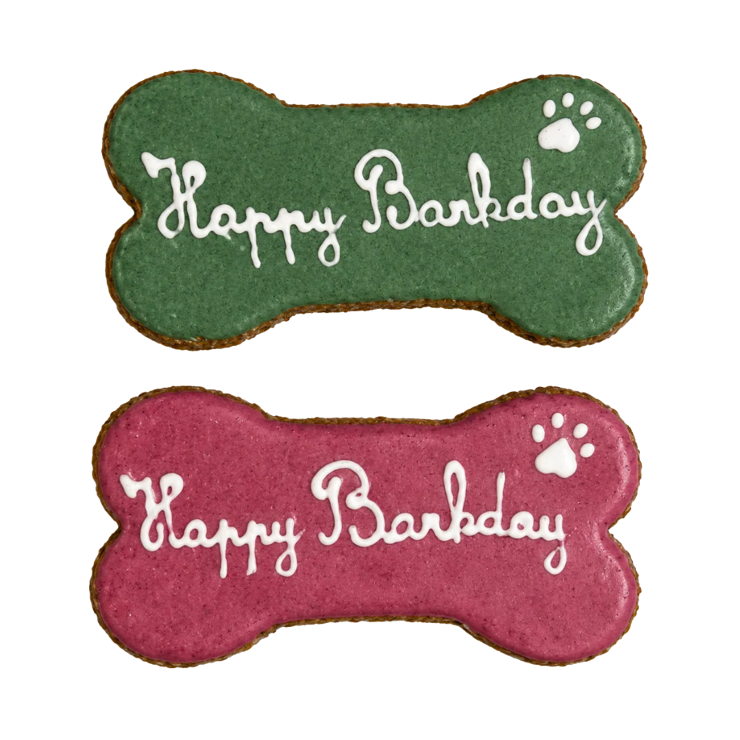 Zwei Hundekeks‑Geburtstagsleckereien in Knochenform mit grüner und roter Glasur und weißem Schriftzug „Happy Barkday“, 
