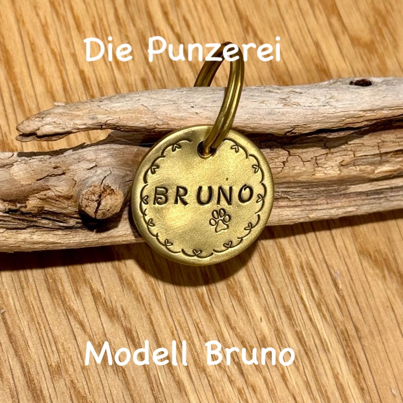 Handgepunzte Hundemarke aus Messing mit Namen „Bruno“ und Rankenmotiv, rundes  Design an Schlüsselring befestigt, präsentiert auf Holzuntergrund