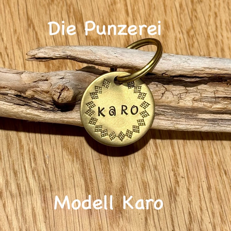 Handgepunzte Hundemarke aus Messing mit Namen „Karo“ und Karomotiv, rundes  Design an Schlüsselring befestigt, präsentiert auf Holzuntergrund