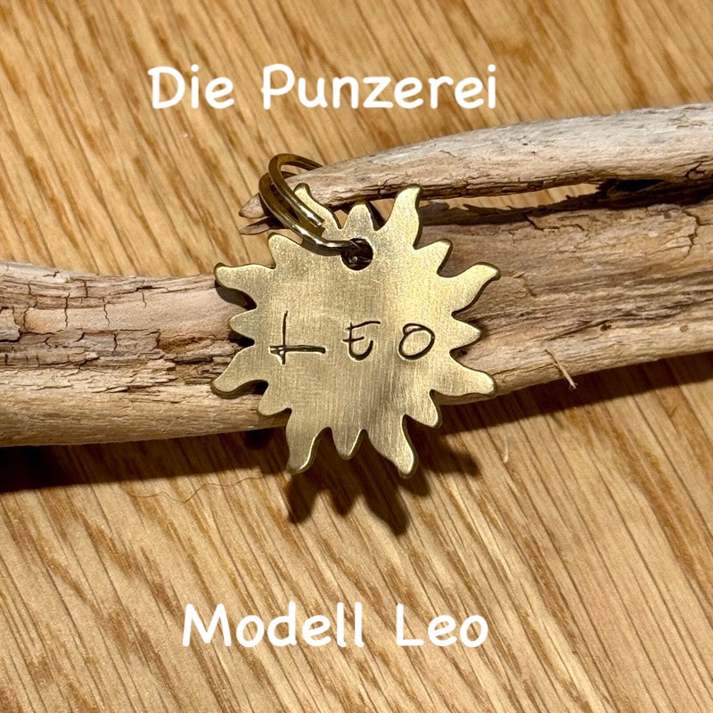 Handgepunzte Hundemarke aus Messing mit Namen „Leo“ sonnenförmiges Design an Schlüsselring befestigt, präsentiert auf Holzuntergrund
