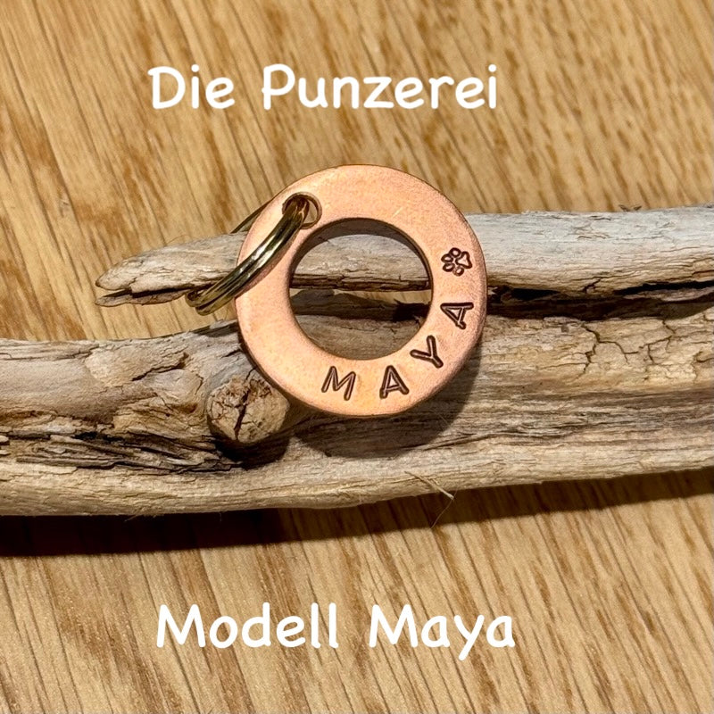 Handgepunzte Hundemarke aus Kupfer mit Namen „Maya“ und Pfotenmotiv, rundes Design an Schlüsselring befestigt, präsentiert auf Holzuntergrund