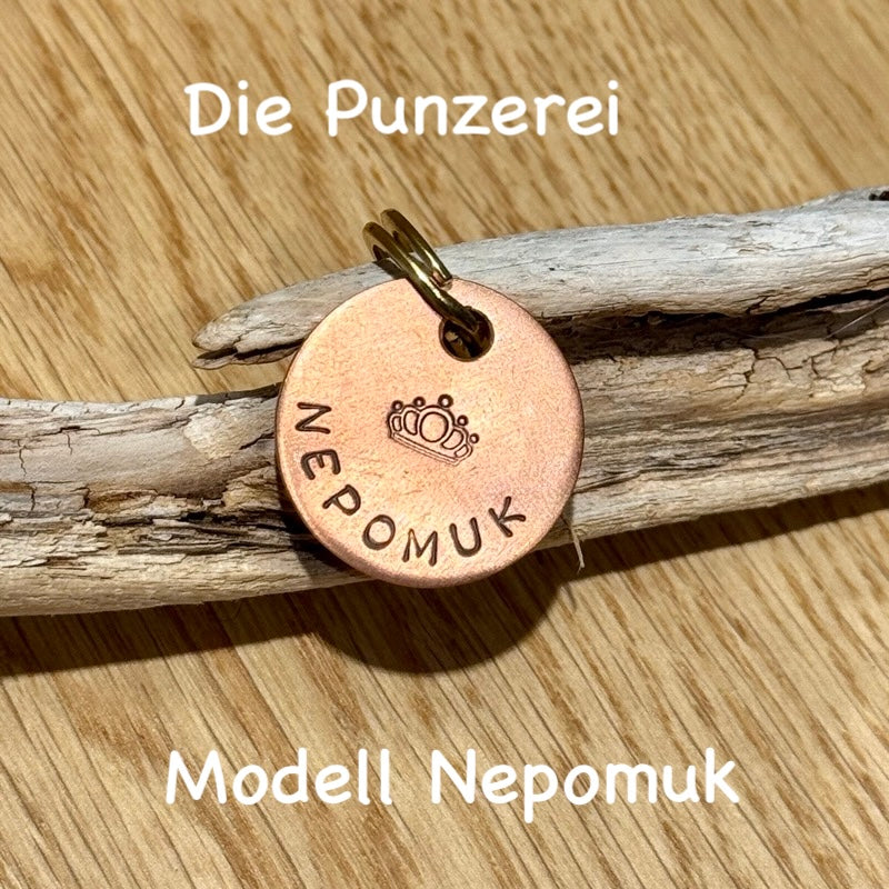 Handgepunzte Hundemarke aus Kupfer mit Namen „Nepomuk“ und Kronenmotiv, rundes Design an Schlüsselring befestigt, präsentiert auf Holzuntergrund