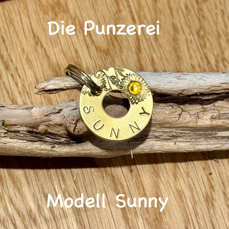 Handgepunzte Hundemarke aus Messing mit Namen „Sonny“ und Pfotenmotiv, ringförmiges Design an Schlüsselring befestigt, präsentiert auf Holzuntergrund