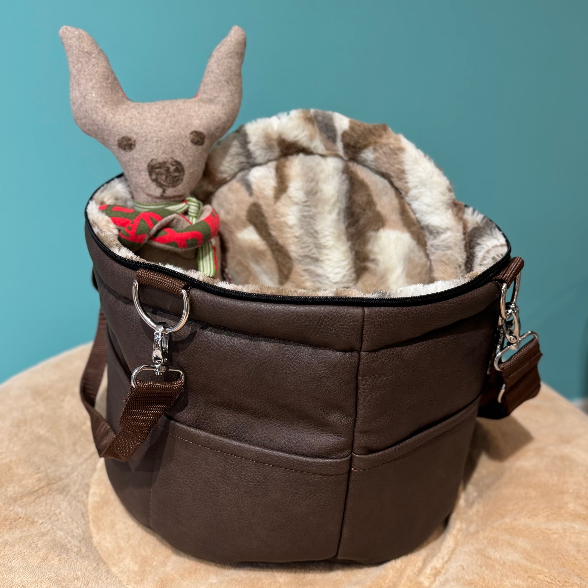 Isarhund Herzflug Tasche in Braun mit flauschigem Kunstfell-Rand und weichem Innenfutter, inklusive herausnehmbarer Netzeinsätze und verstellbarem Schultergurt, komfortable Hundetragetasche für kleine Hunde. Ein Spielzeughund sitzt in der Tasche.