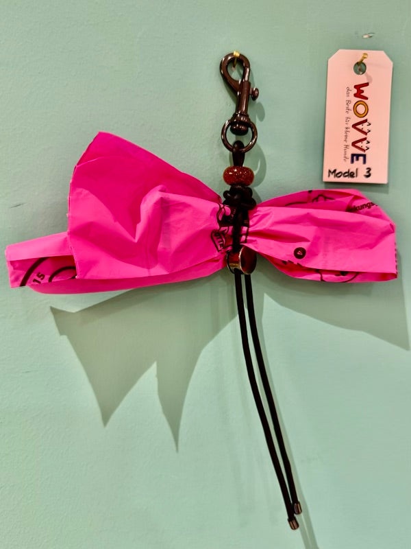 Handgefertigter Isarhund Kotbeutelhalter aus Leder mit schwarzem Karabinerhaken, befestigt an einer Wand, mit pinken Kotbeuteln und Markenanhänger, Made in Bavaria