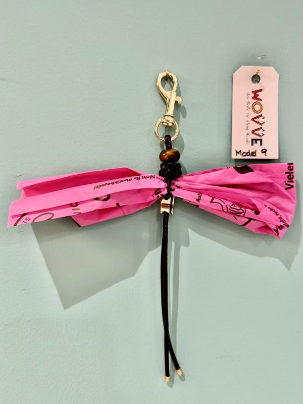 Handgefertigter Isarhund Kotbeutelhalter aus Leder mit goldfarbenem Karabinerhaken, befestigt an einer Wand, mit pinken Kotbeuteln und Markenanhänger, Made in Bavaria