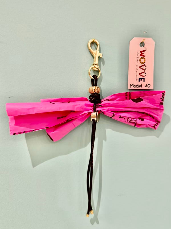 Handgefertigter Isarhund Kotbeutelhalter aus Leder mit goldfarbenem Karabinerhaken, befestigt an einer Wand, mit pinken Kotbeuteln und Markenanhänger, Made in Bavaria