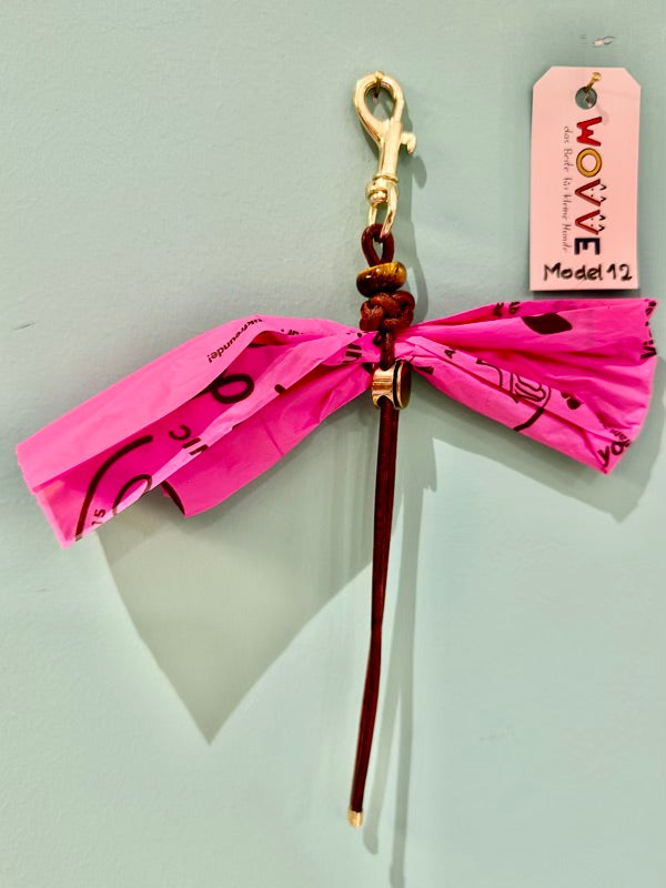 Handgefertigter Isarhund Kotbeutelhalter aus Leder mit goldfarbenem Karabinerhaken, befestigt an einer Wand, mit pinken Kotbeuteln und Markenanhänger, Made in Bavaria