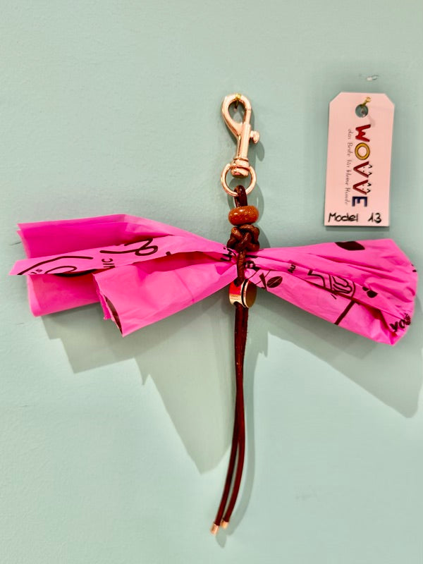 Handgefertigter Isarhund Kotbeutelhalter aus Leder mit goldfarbenem Karabinerhaken, befestigt an einer Wand, mit pinken Kotbeuteln und Markenanhänger, Made in Bavaria