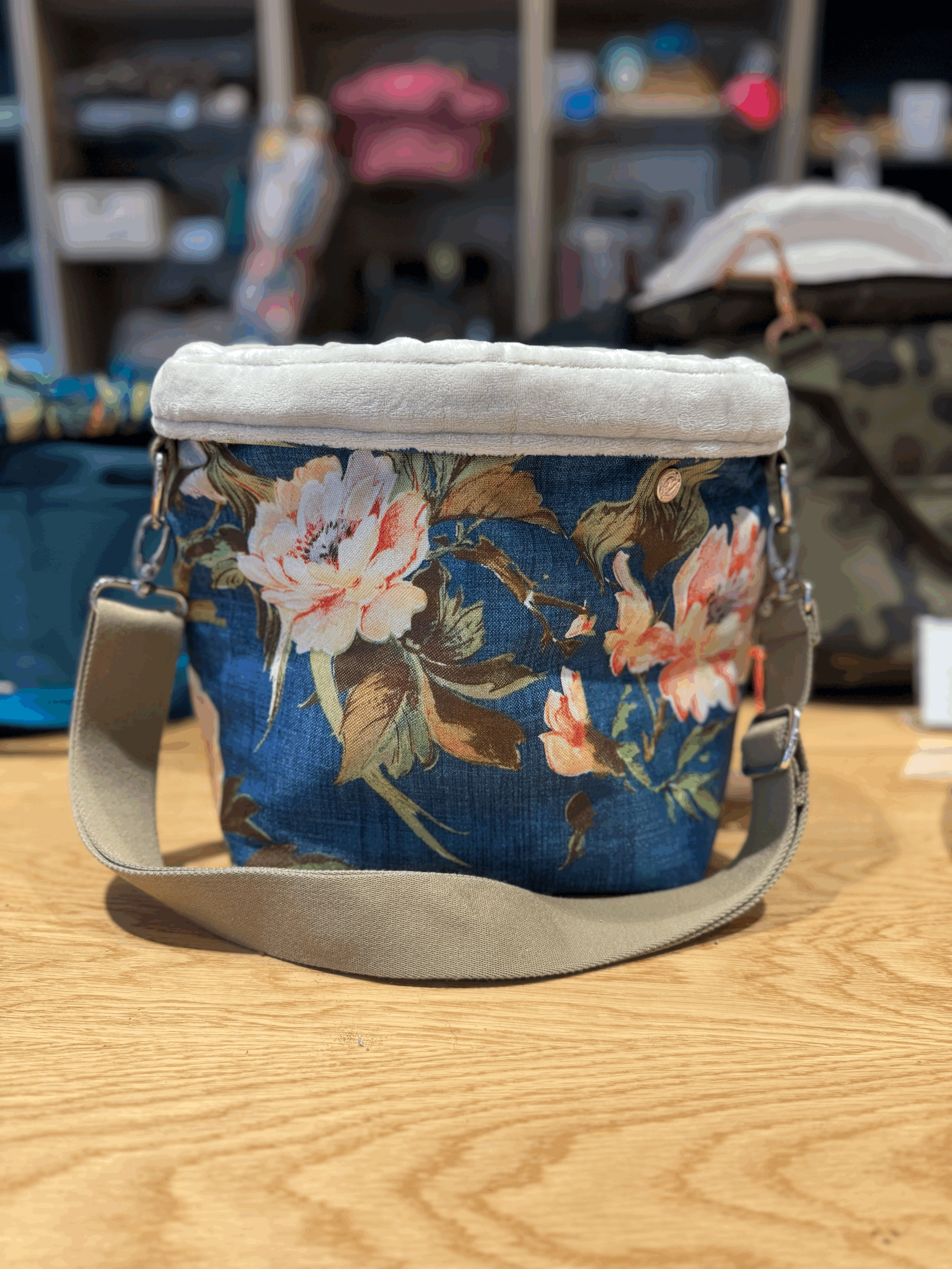Känguru-Tragetasche für kleine Hunde in blauem Stoff mit floralen Blütenmotiven, gepolstertem Rand und verstellbarem Schultergurt, auf Holztisch präsentiert.