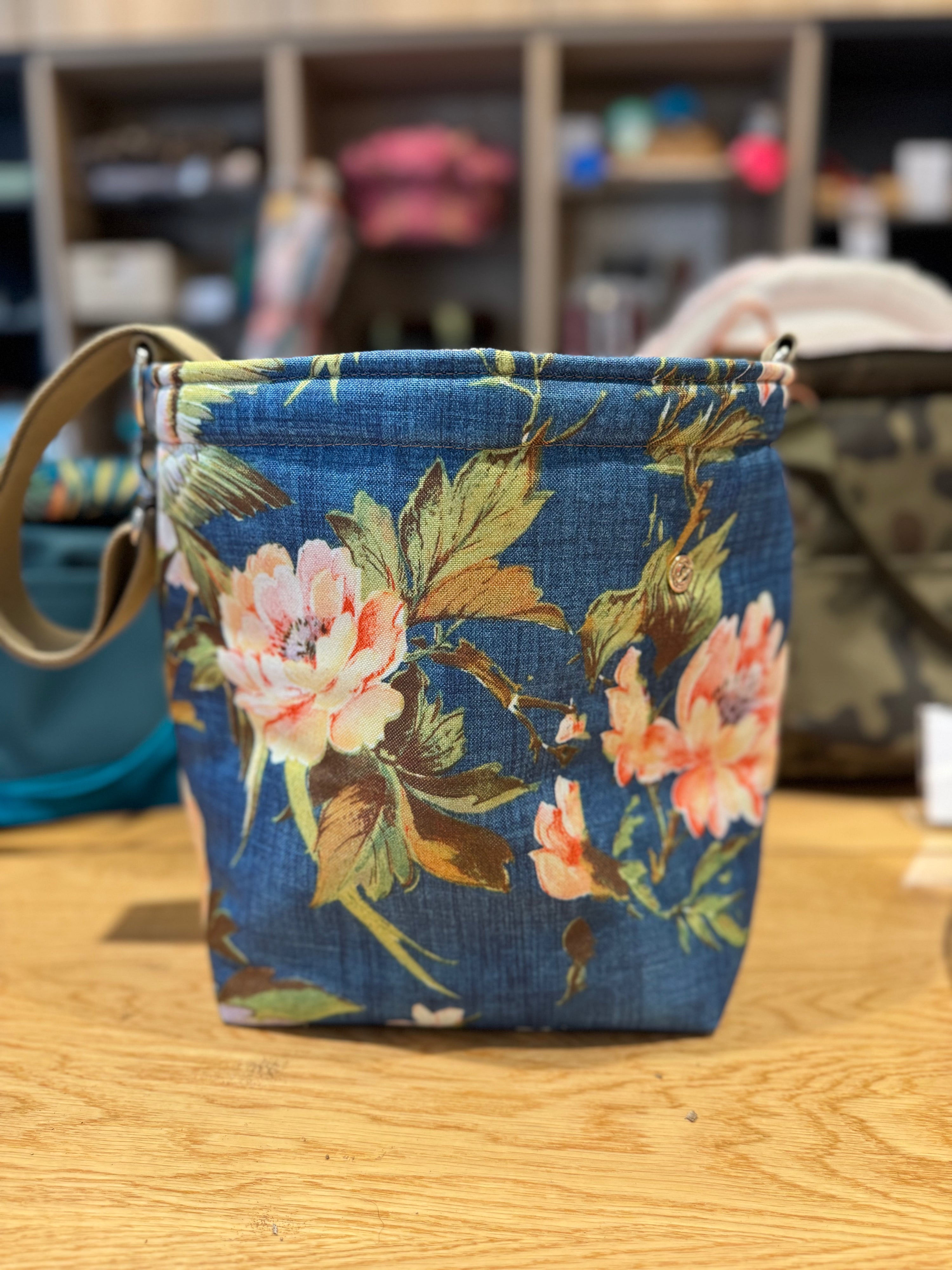 Känguru-Tragetasche für kleine Hunde aus blauem Stoff mit floralen Blütenmotiven, gerade frontal aufgenommen auf einem Holztisch.“