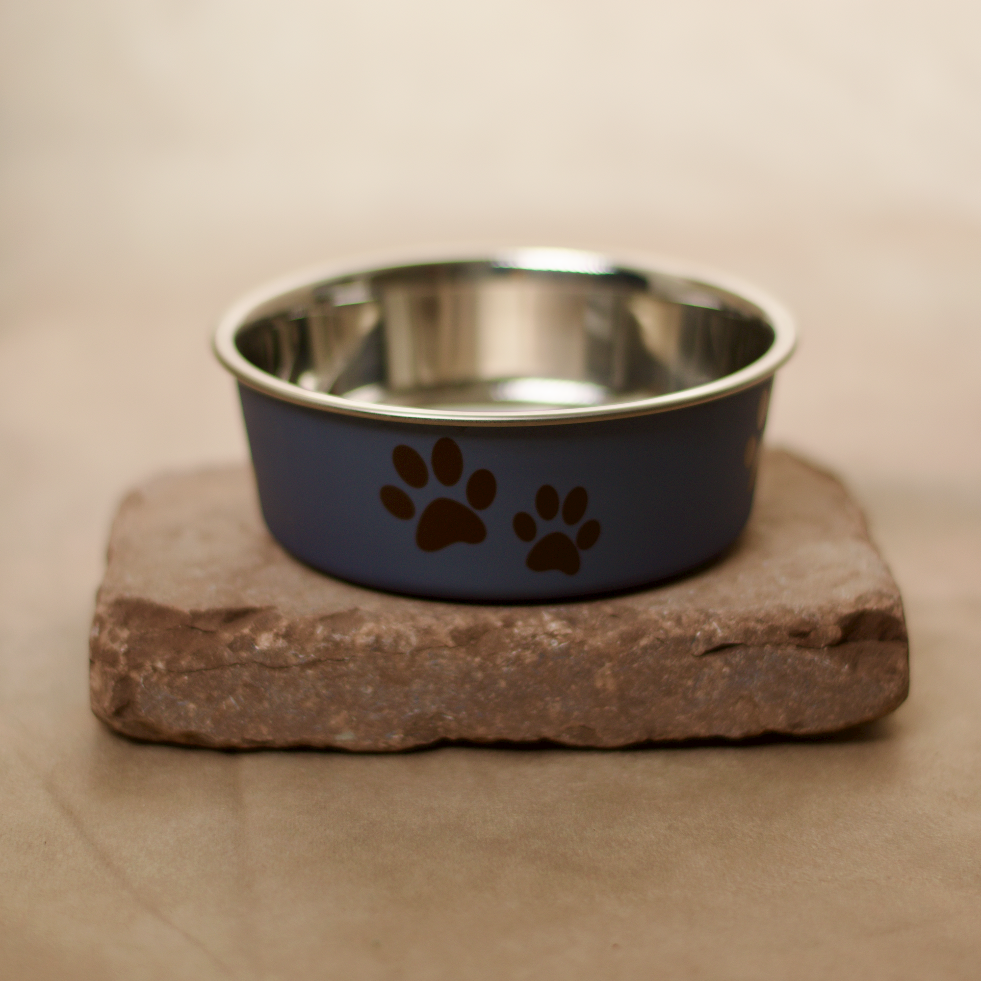 Dunkelblauer Edelstahl Futternapf für Hunde und Katzen, mit Anti-Rutsch Gummiring am Boden, niedlicher Print ringsum, für Nass-, Trockenfutter oder Wasser verwendbar. Auf einem flachen Stein präsentiert.