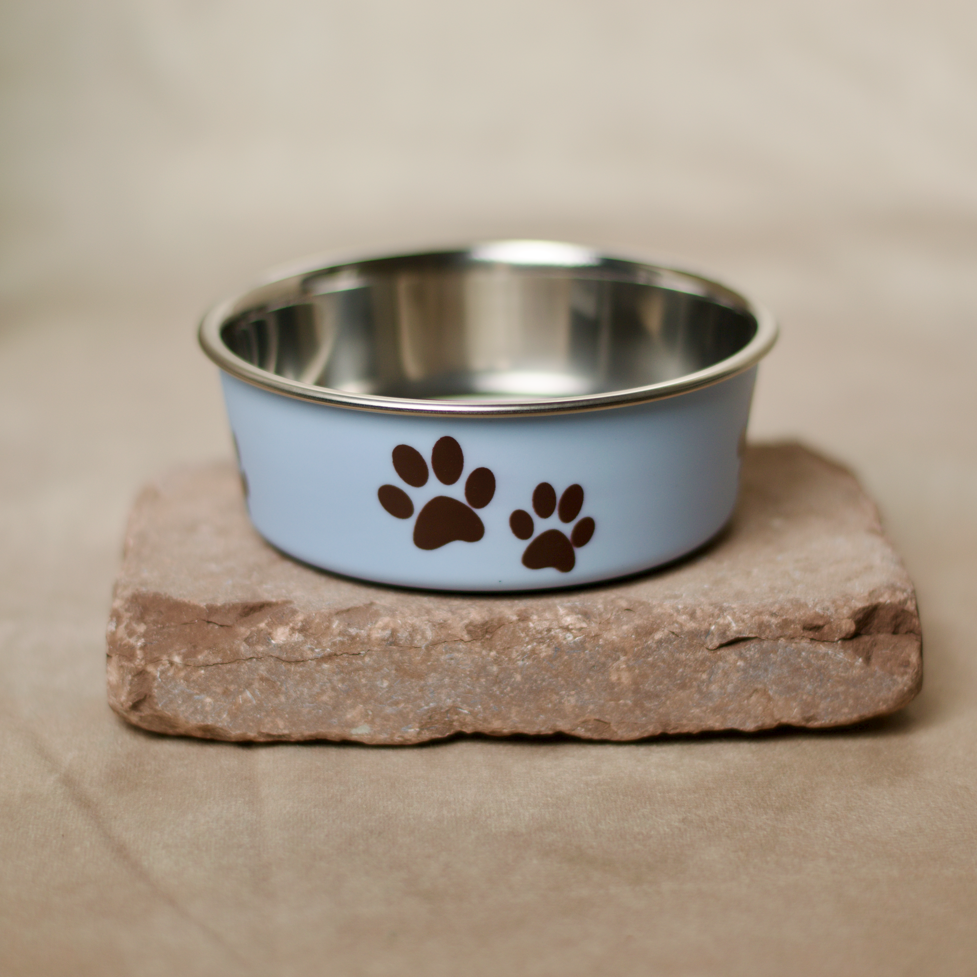 Hellblauer Edelstahl Futternapf für Hunde und Katzen, mit Anti-Rutsch Gummiring am Boden, niedlicher Print ringsum, für Nass-, Trockenfutter oder Wasser verwendbar. Auf einem flachen Stein präsentiert.