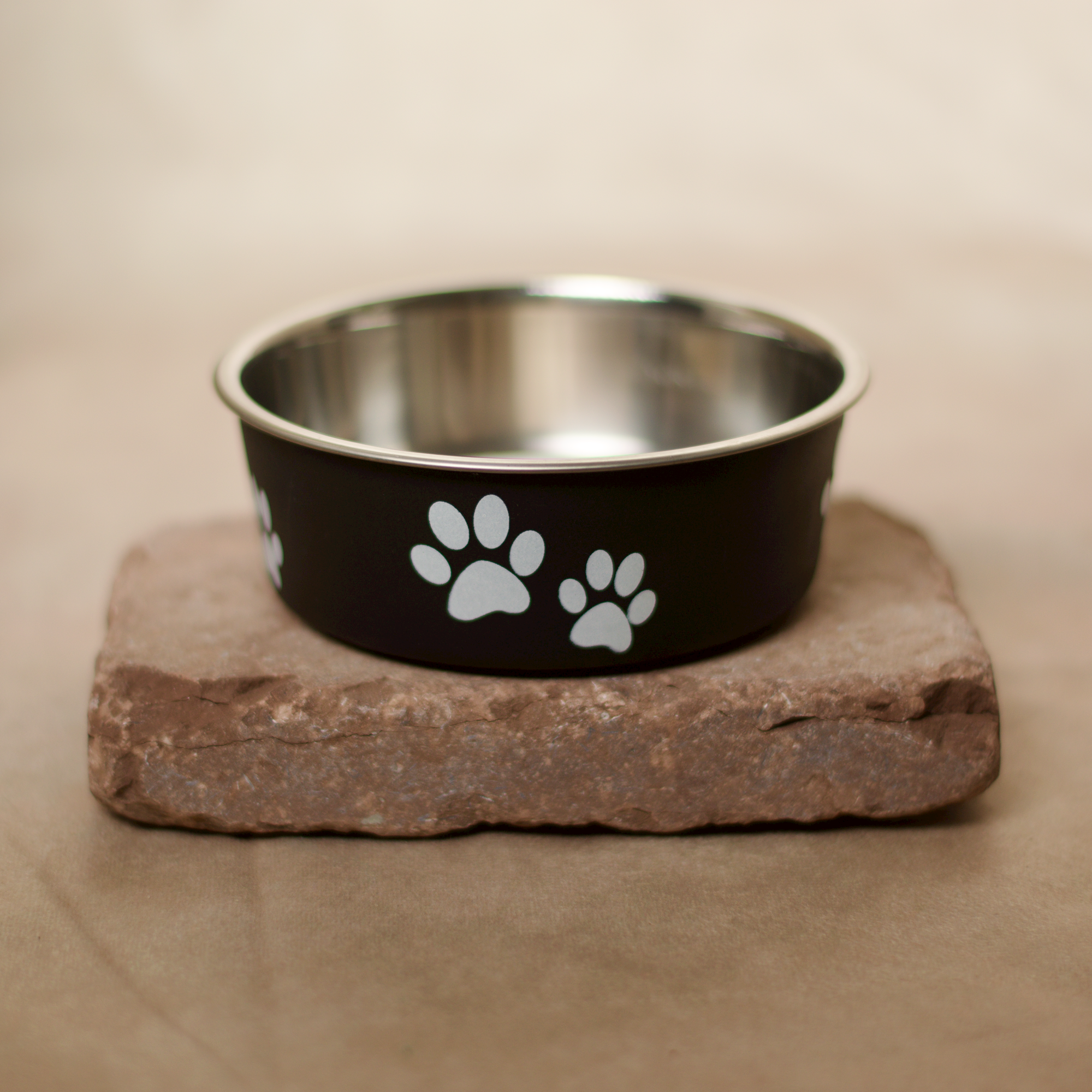 Schwarzer Edelstahl Futternapf für Hunde und Katzen, mit Anti-Rutsch Gummiring am Boden, niedlicher Print ringsum, für Nass-, Trockenfutter oder Wasser verwendbar. Auf einem flachen Stein präsentiert.