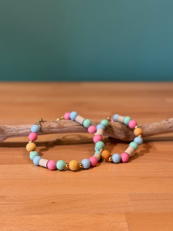 „Bunte Anti-Zecken-Halsketten für Hunde aus Holz- und Kunststoffperlen in Pastellfarben auf Holzstück, dekorativ arrangiert“
