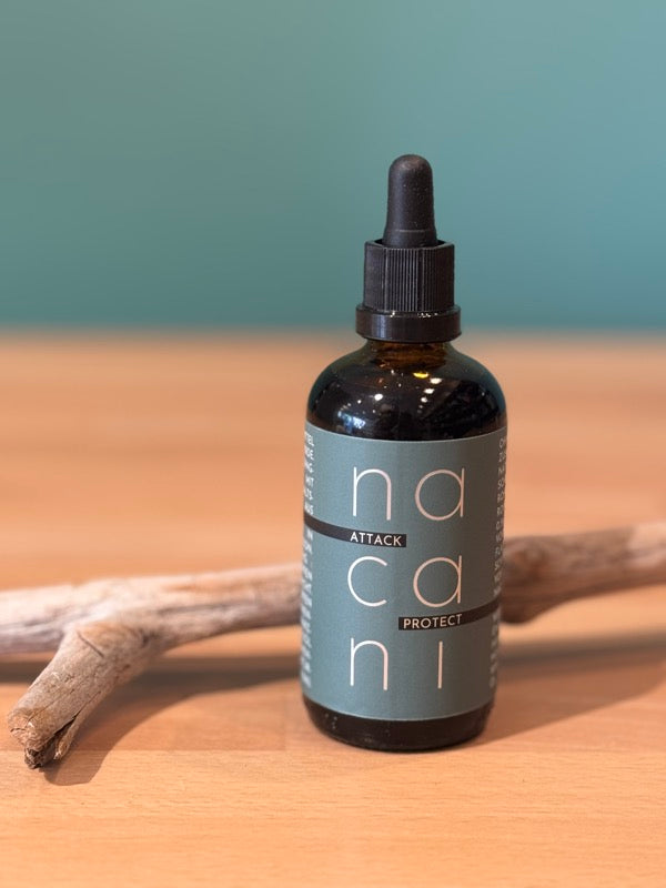 „Nacani Attack Protect Zeckenschutz-Öl für Hunde in dunkler Glasflasche mit Pipette auf Holzunterlage vor grünem Hintergrund“