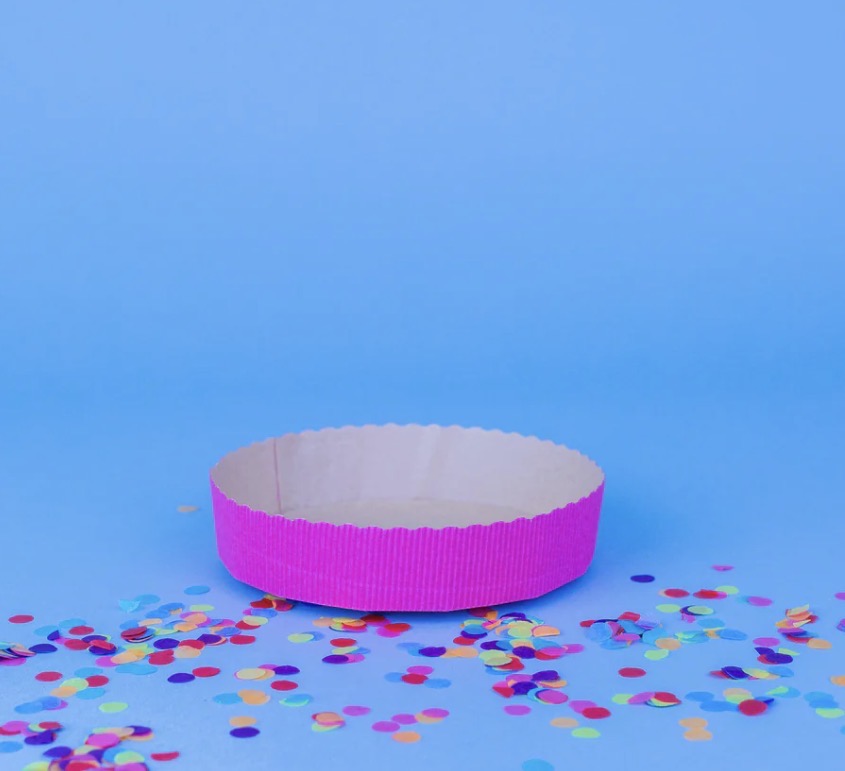 Eine pinke Kuchenbackform bei einem blauen Hintergrund mit Konfetti 