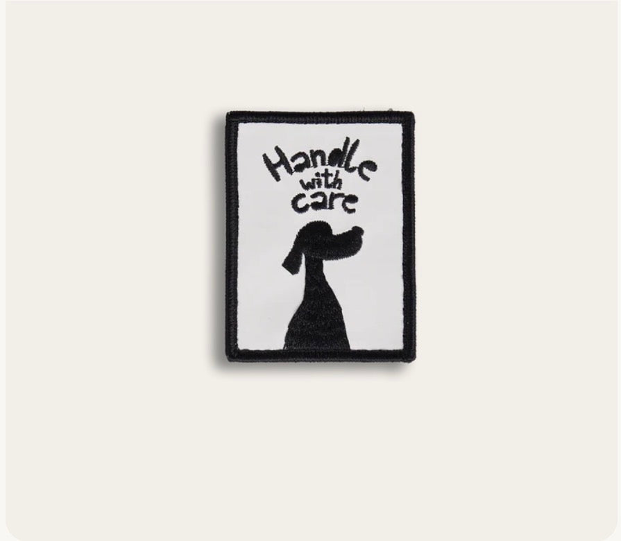 Rechteckiger, gestickter Aufnäher mit schwarzer Hundesilhoutte und dem Schriffzug „Handle with care“