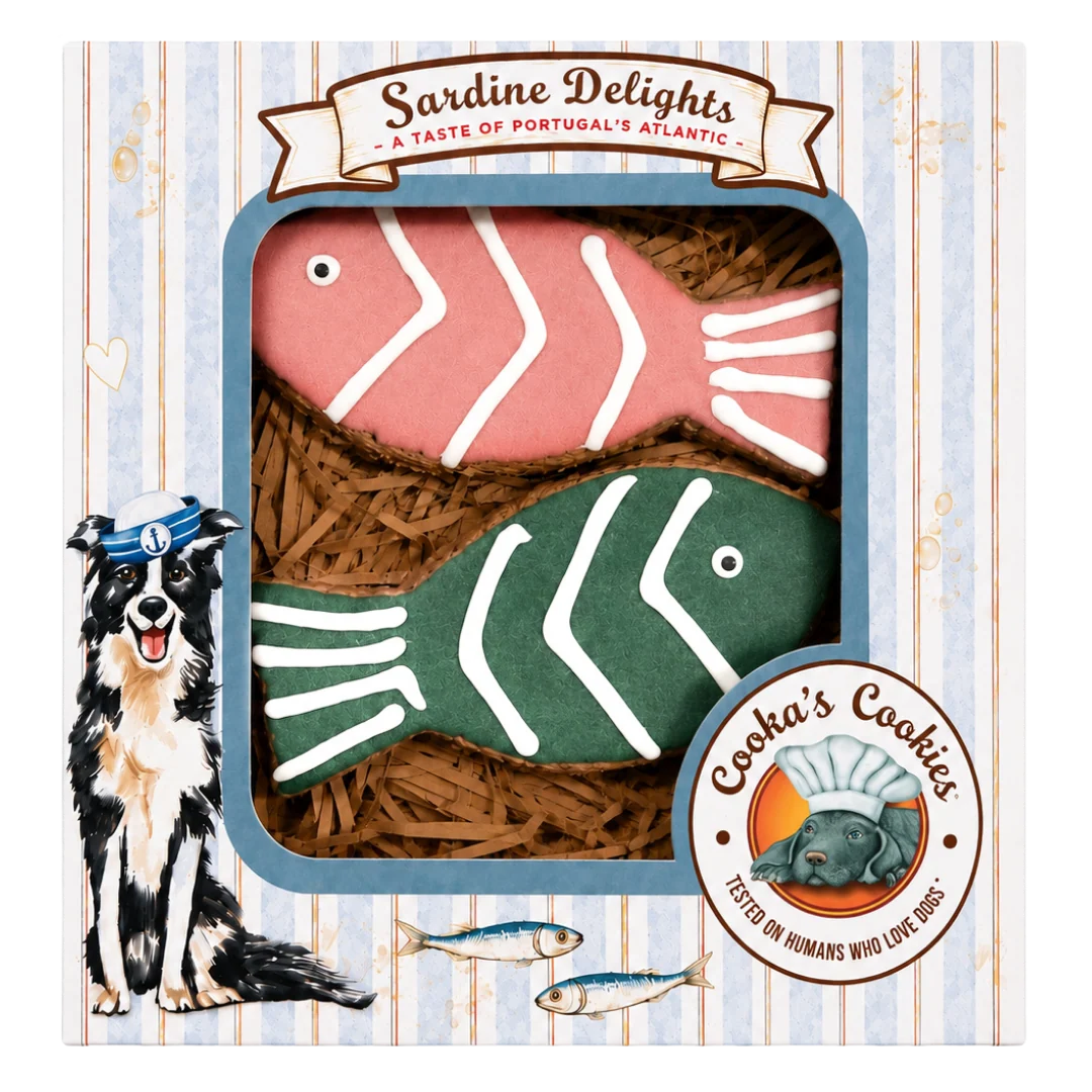 Produktfoto: Verpackung „Sardine Delights – A Taste of Portugal’s Atlantic“ mit zwei fischförmigen Hundekeksen (rosa und grün, weiß verziert) auf Holzwolle. Links Illustration eines Hundes mit Matrosenmütze, unten rechts rundes Logo „Cooka’s Cookies – Tested on Humans Who Love Dogs“ vor hellblau‑weiß gestreiftem Hintergrund mit kleinen Herzen und Blasen.
