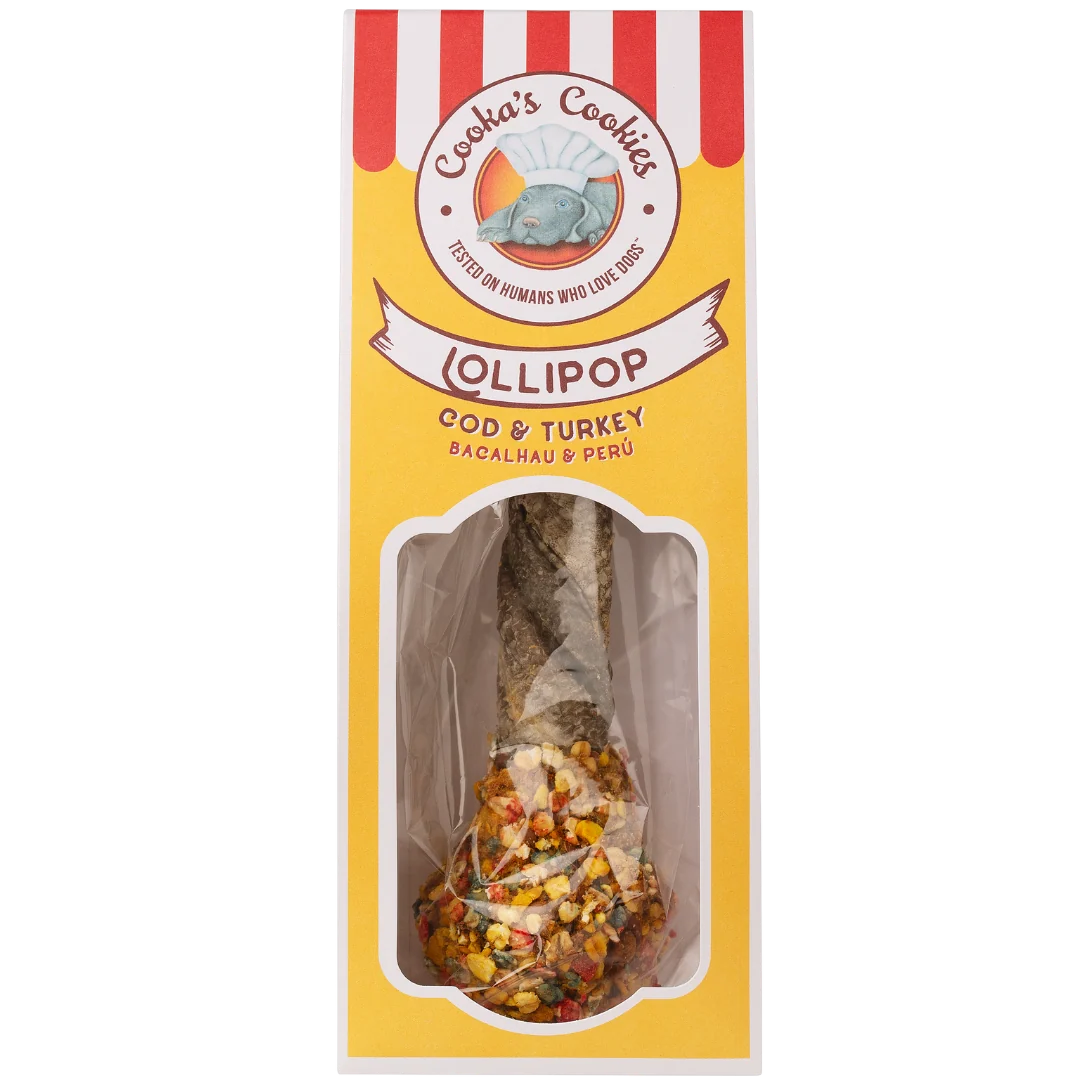 Gelb verpacktes Hundeleckerli in Lollipop‑Form mit bunten Stückchen, „Cooka’s Cookies“-Branding und Hund mit Kochmütze auf rot‑weiß gestreiftem Hintergrund.